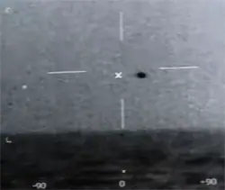 Public-domain still from the USS Omaha UAP video showing a small dark object on a sensor display